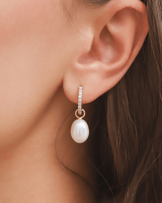 An earring with a gold huggie, small gems, and a drop pearl on a model's ear.