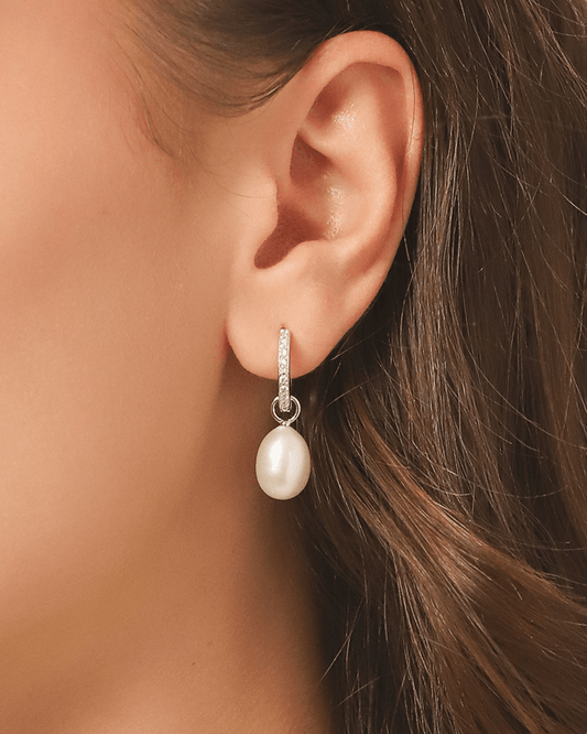 A close-up of an earlobe adorned with a pearl drop earring, featuring a silver hoop.