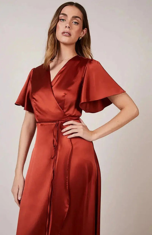 Woman wearing a red burnt orange satin bridesmaid dress against a neutral background