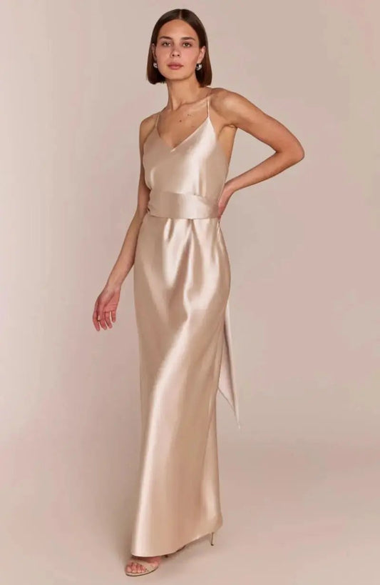 Woman wearing a long, light-colored satin champagne Bridesmaid dress against a plain background