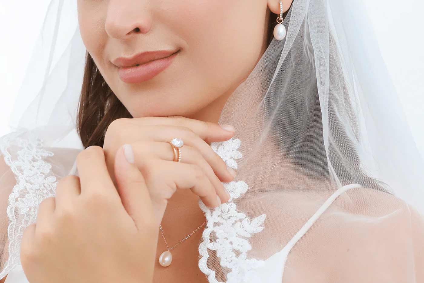 Close up of a bride wearing pearl earrings, pearl necklace and gold ring