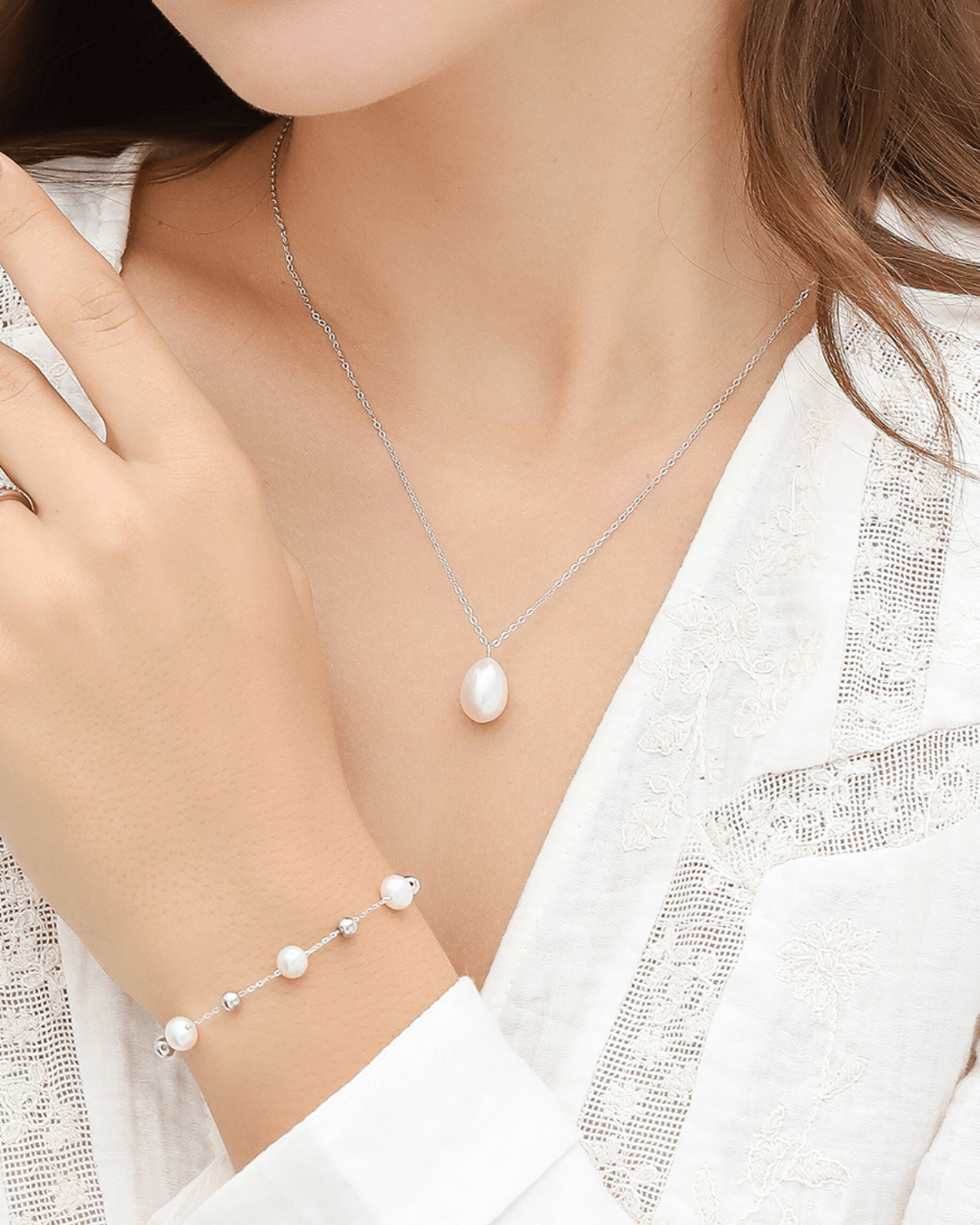 A woman's chest and arm, wearing a pearl pendant necklace and a pearl bracelet.
