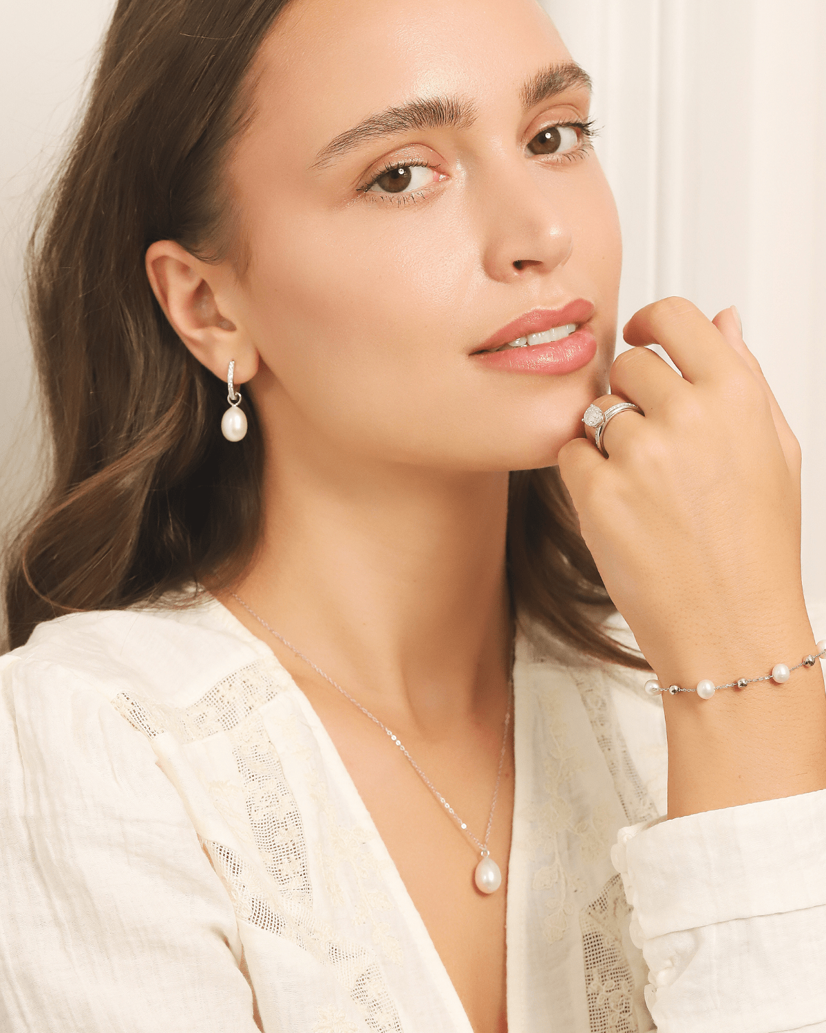 A woman wearing a matching set of pearl earrings, necklace, bracelet, and ring.
