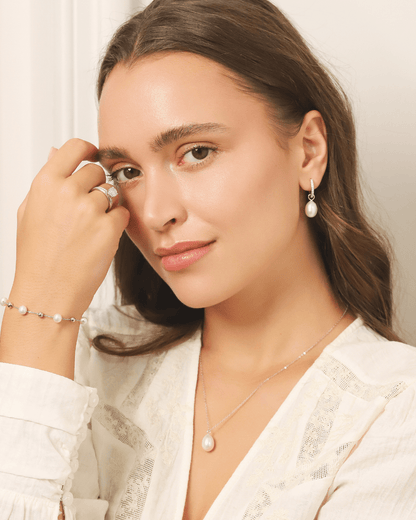 A model wearing a pearl pendant necklace, pearl drop earrings, and pearl bracelet.