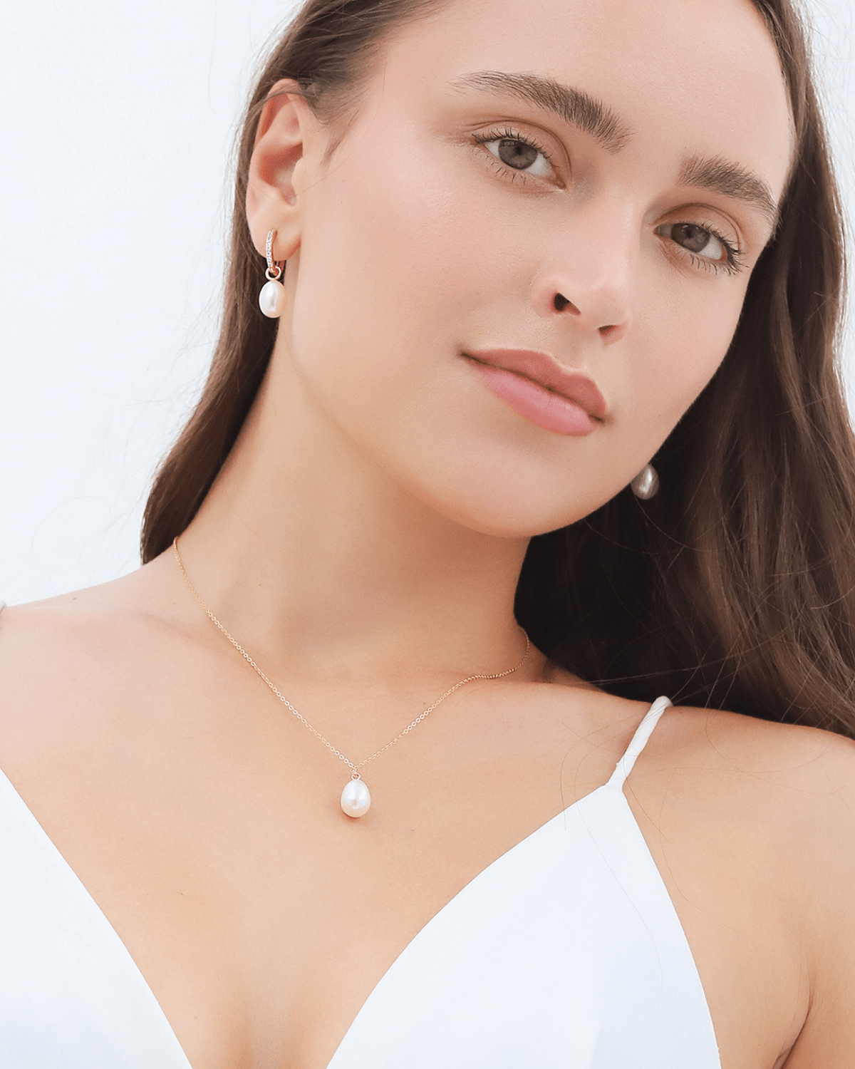 A woman wearing a pearl pendant necklace and small hoop pearl earrings, looking forward.