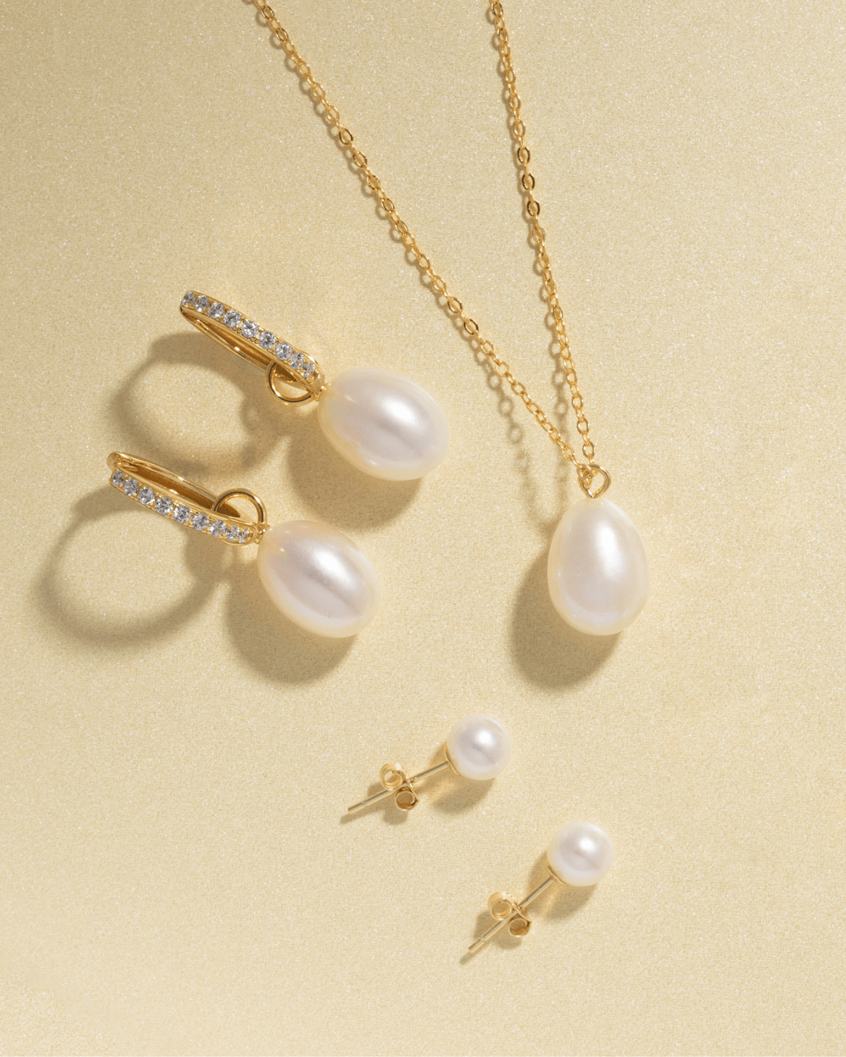 A set of gold pearl jewelry: earrings, necklace, and two small stud earrings.