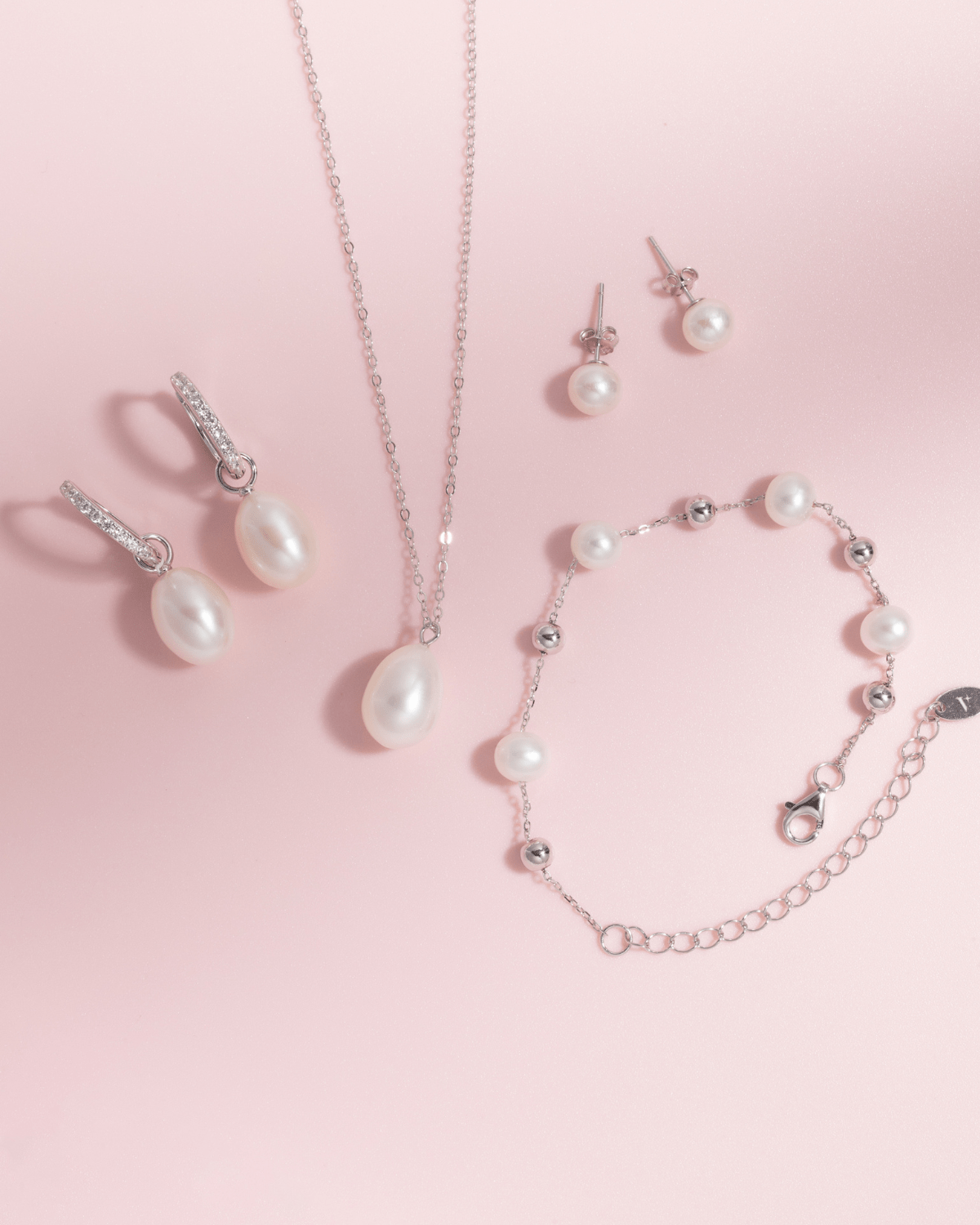 A full set of pearl jewelry on a pink background, including earrings, necklace, and bracelet.