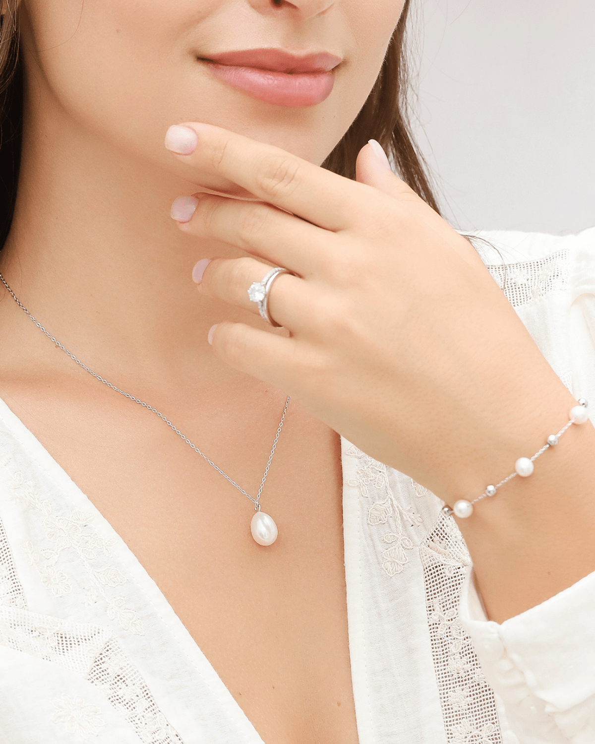 A close-up of a model wearing a pearl pendant necklace, pearl bracelet, and ring.