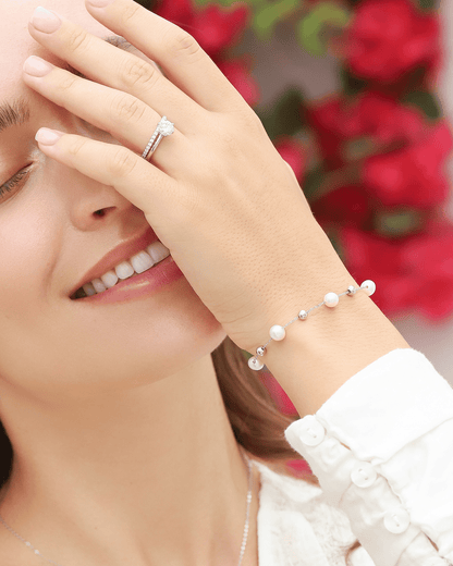 A woman wearing a pearl bracelet, ring, and smiling, covering half of her face.