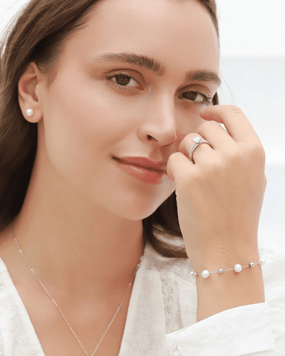 A woman wearing a white pearl bracelet and ring, looking directly at the camera.