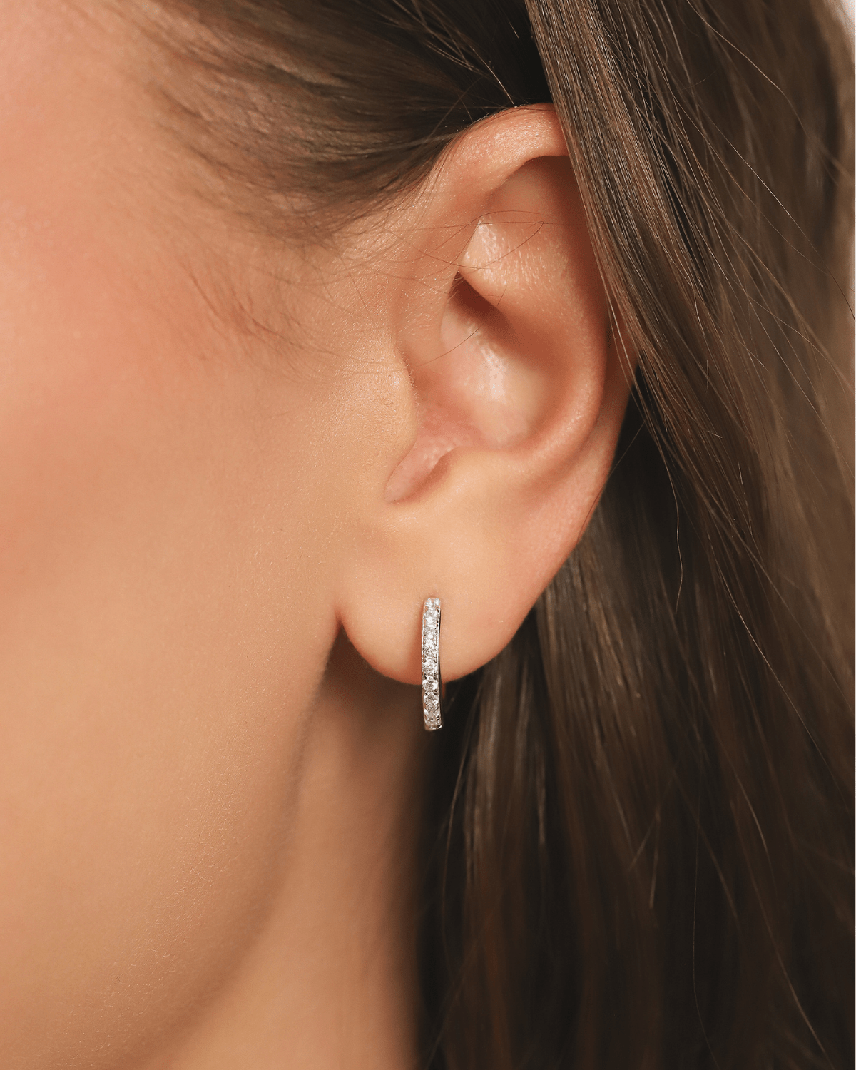 A close-up of an earlobe adorned with a delicate, gem-encrusted silver hoop earring.