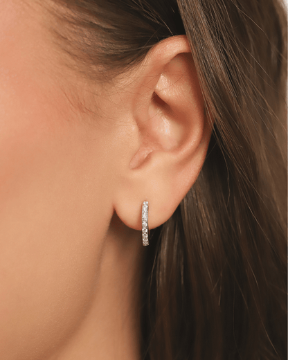 A close-up of an earlobe adorned with a delicate, gem-encrusted silver hoop earring.