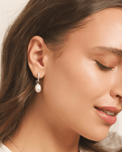 A woman's profile, showcasing a pearl drop earring and a subtle necklace.
