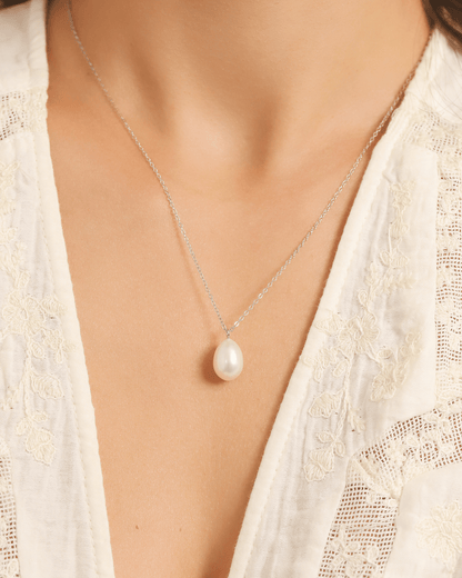 A close-up of a model's chest wearing a white pearl pendant necklace.