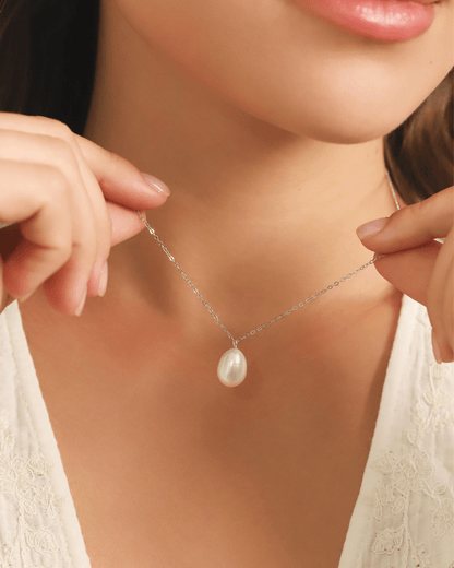 A close-up of a model wearing a white pearl pendant necklace with a silver chain.