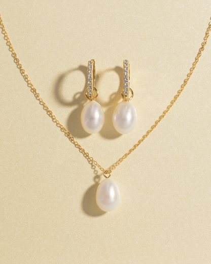 A pearl pendant necklace and matching hoop earrings with pearls on a light background.