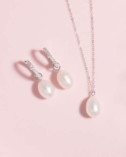 A pearl pendant necklace and pearl drop earrings on a pink background.