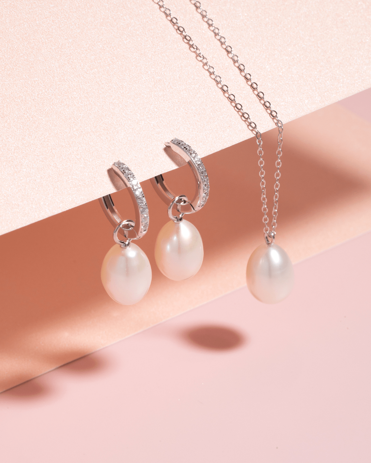 A pearl necklace and matching pearl drop earrings artfully arranged on a pink surface.