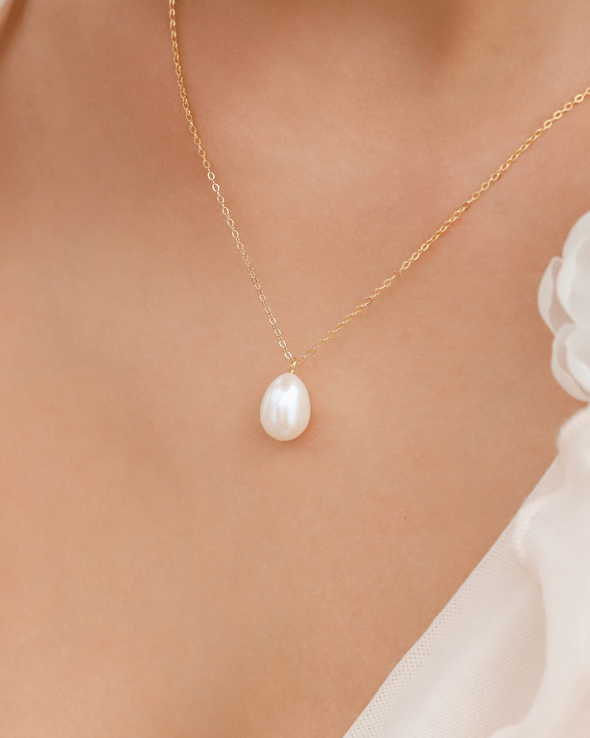Close-up of a person's décolletage wearing a pearl pendant on a gold chain.