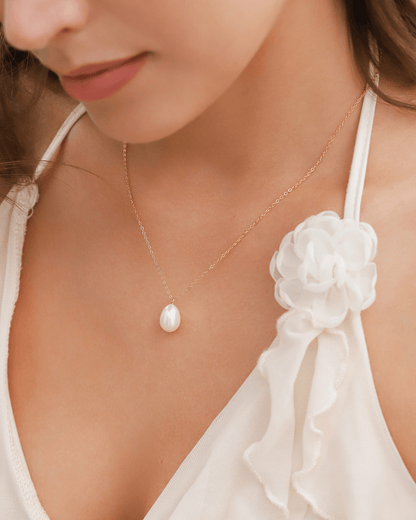 Close-up of a person's chest wearing a subtle pearl necklace, with a white flower accent.