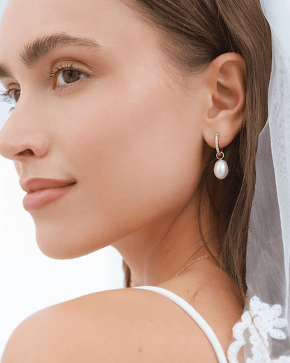A bride wearing a gold huggie earring with gems and a pearl drop, looking right.