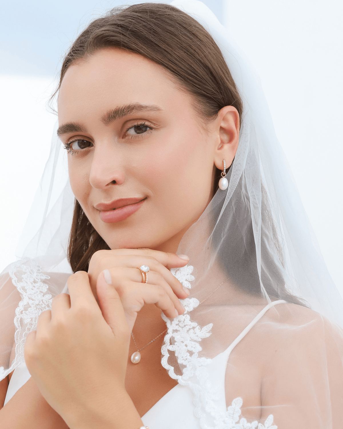 A bride wearing a veil and a gold pearl earring, looking at the viewer.