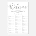 A wedding reception welcome seat plan sign with elegant silver script and serif text on a white background, displayed against a light gray backdrop.