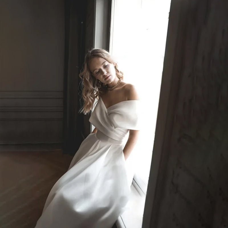 Bride wearing the A-Line Ankle-Length Off-The-Shoulder Wedding Dress side-view sat on a window ledge