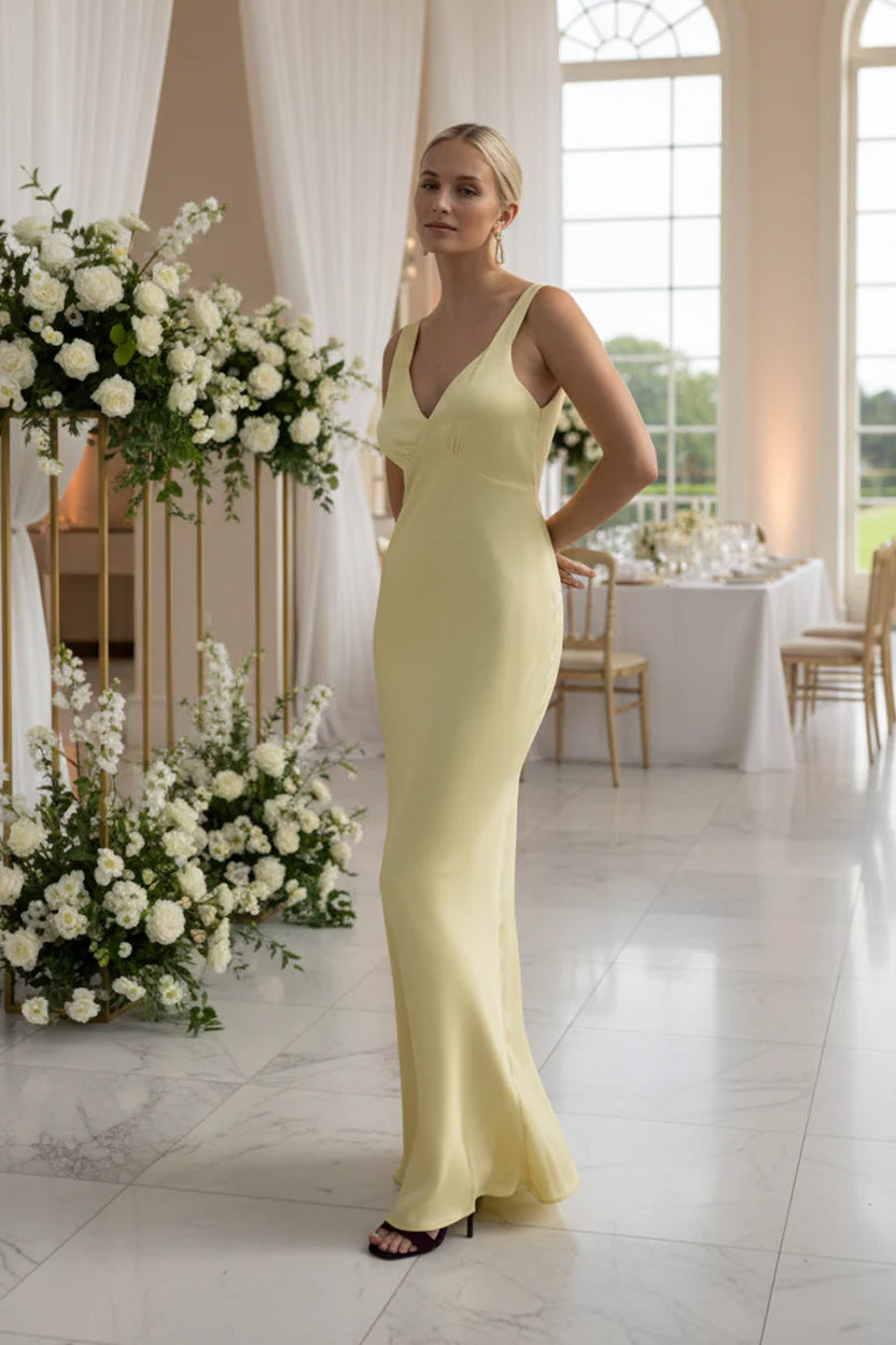 Bridesmaid in a lemon yellow evening bridesmaid gown standing in a decorated room at a wedding venue with floral arrangements.