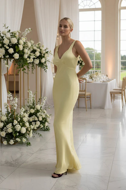 Bridesmaid in a lemon yellow evening bridesmaid gown standing in a decorated room at a wedding venue with floral arrangements.