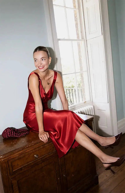 Woman in a red satin bridesmaid dress sitting on a wooden dresser by a window.