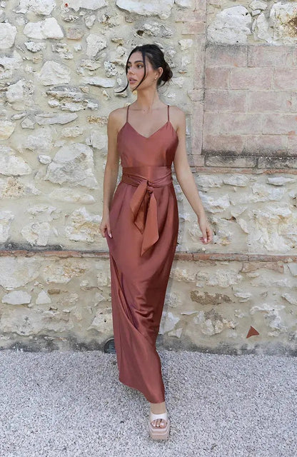 Woman in a rust-colored terracotta brown bridesmaid dress standing against a stone wall.