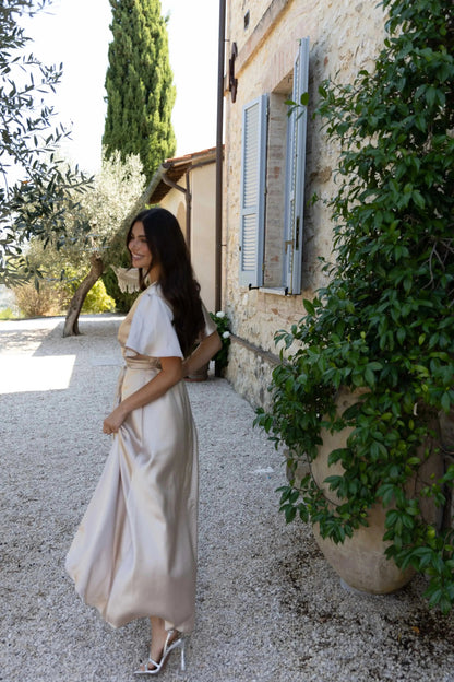 Woman in a champagne bridesmaid dress standing in front of a stone building with greenery.
