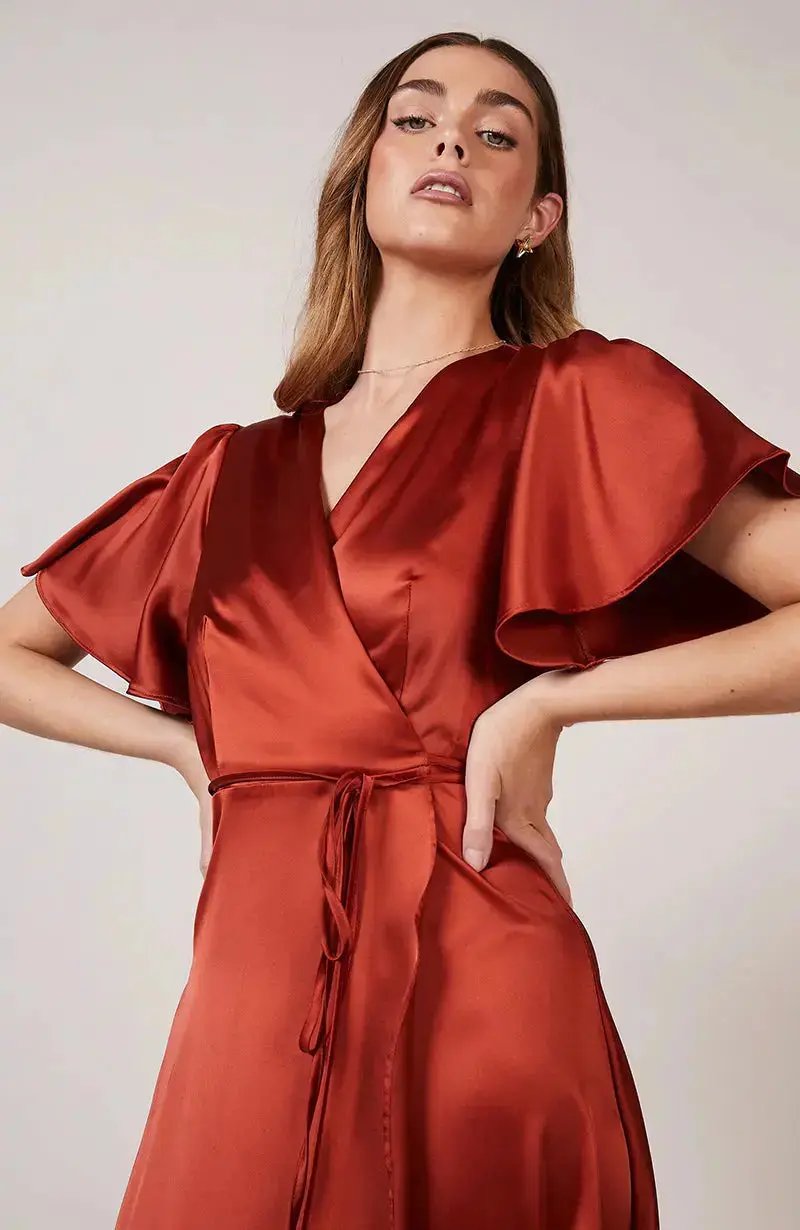 Woman wearing a burnt orange satin bridesmaid dress against a plain background