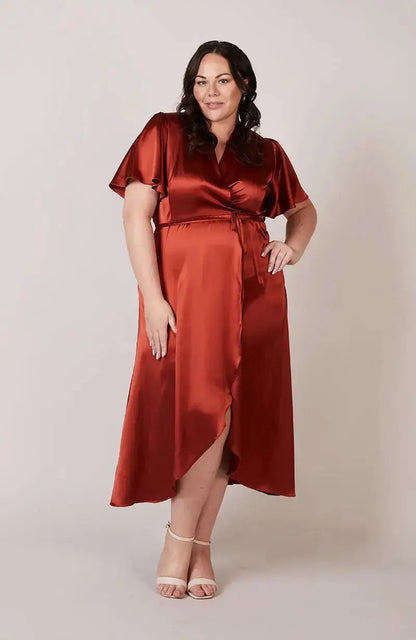 Bridesmaid wearing a burnt orange satin dress against a plain background
