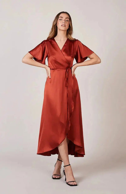 Bridesmaid wearing a burnt orange rust-colored satin dress on a plain background