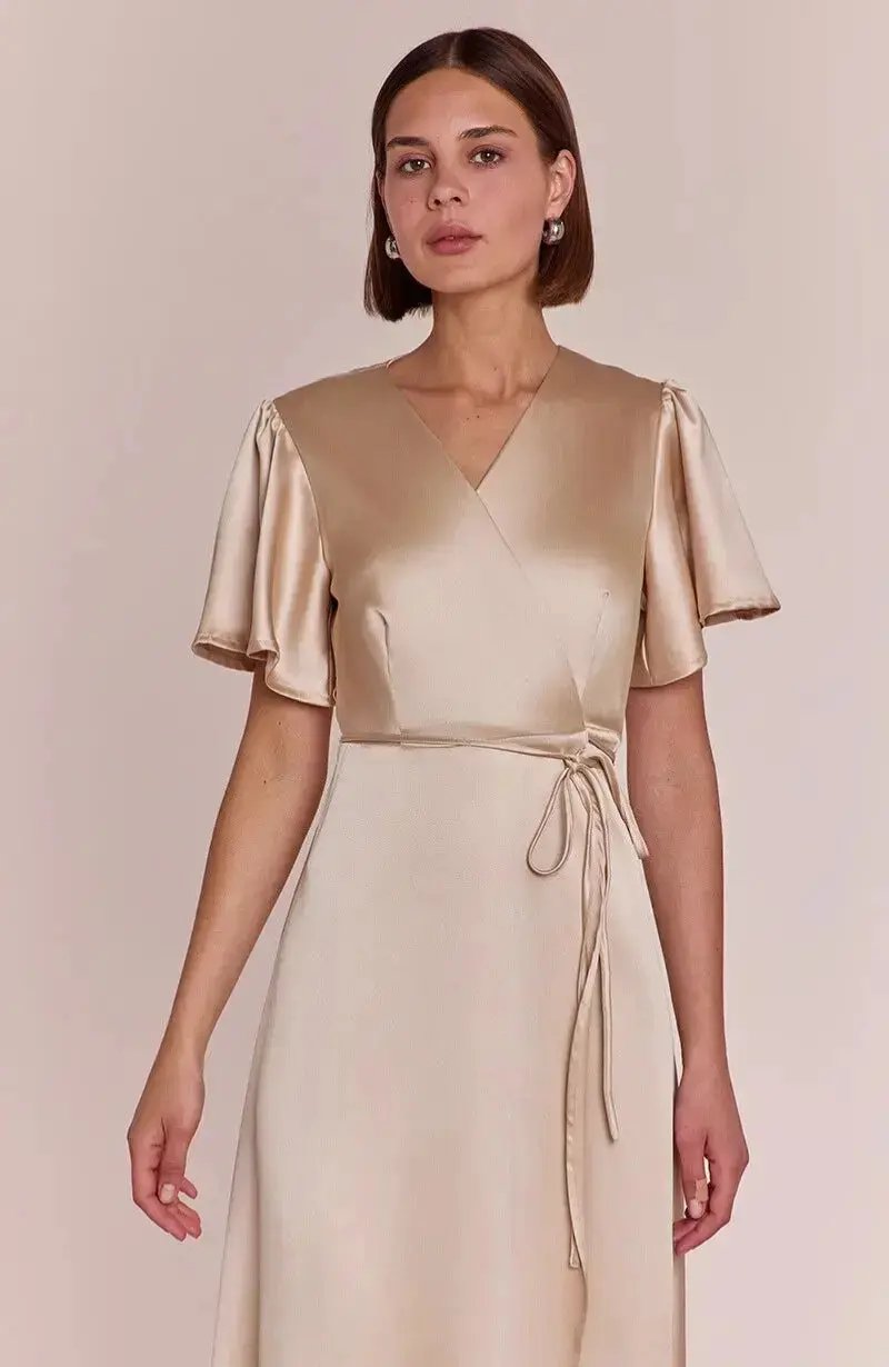 Woman wearing a satin champagne bridesmaid  dress against a plain background
