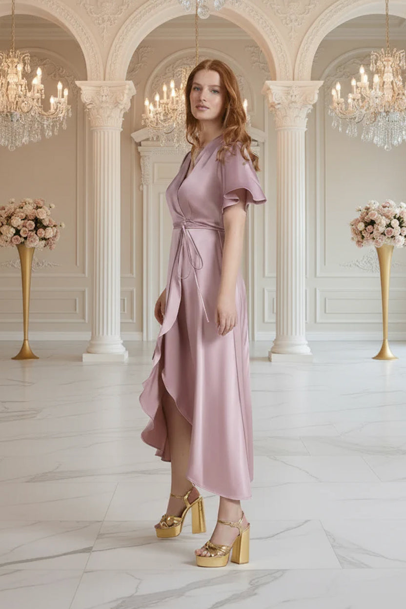Woman in a pink bridesmaid dress standing in an elegant interior setting with chandeliers and floral arrangements.