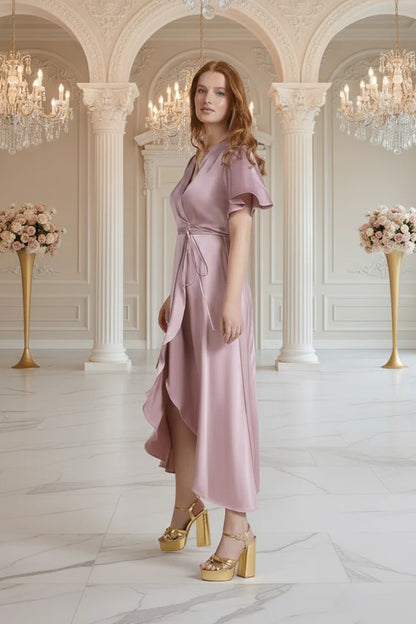 Woman in a pink bridesmaid dress standing in an elegant interior setting with chandeliers and floral arrangements.