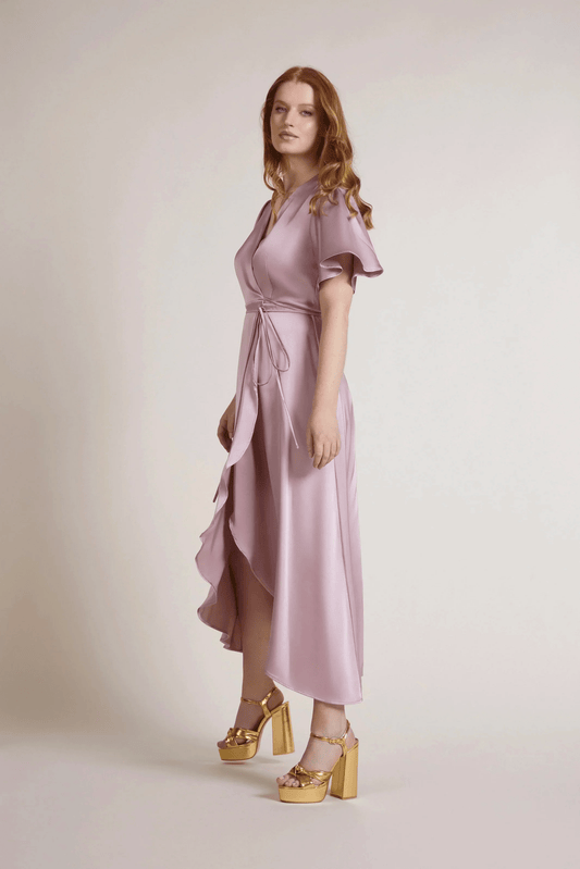 Woman wearing a pink bridesmaid dress with ruffled sleeves and a plain background