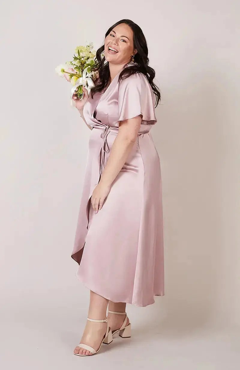 Bridesmaid in a light pink dress holding flowers against a plain background