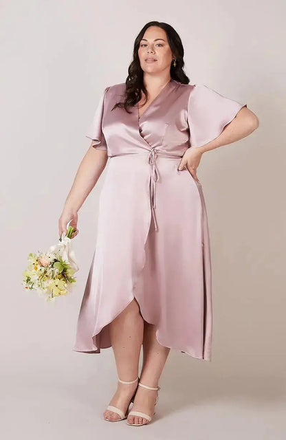 Woman wearing a rose pink satin bridesmaid dress holding flowers against a plain background