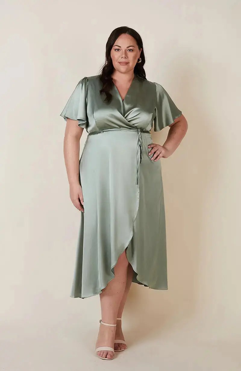 Woman wearing a sage green satin wrap Bridesmaid dress against a plain background