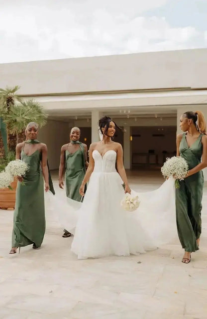 Bride in a white gown with three bridesmaids in olive green bridesmaid dresses outdoors.