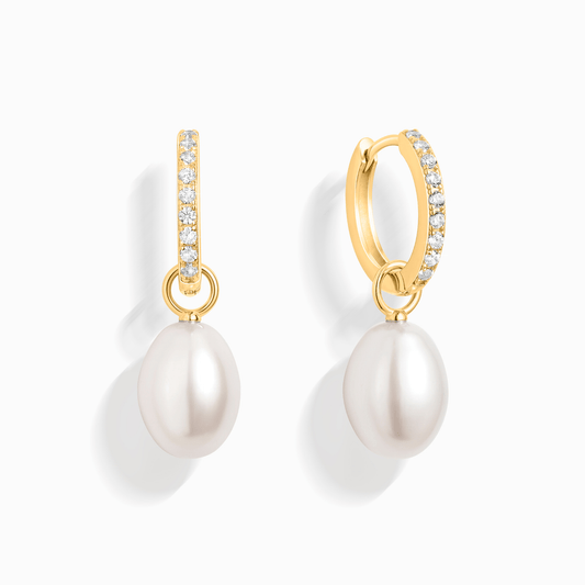 A pair of gold huggie earrings with a line of small gems and a drop pearl.