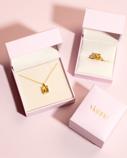 Two pink jewelry boxes with a necklace and ring, and a third box with the brand name.