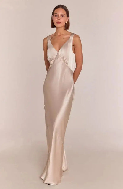 Woman wearing a long, elegant champagne satin bridesmaid dress on a plain background