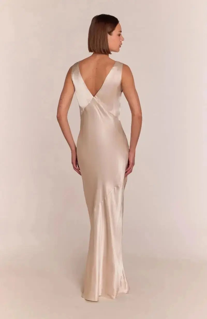 Woman wearing a long, elegant champagne satin bridesmaid dress with a plain background
