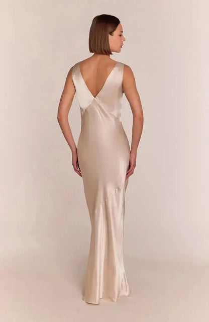 Woman wearing a long, elegant champagne satin bridesmaid dress with a plain background