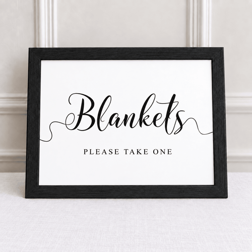 A framed sign with a black wood-look frame and white background, reading 'Blankets' in large script and 'PLEASE TAKE ONE' below, displayed against a light neutral wall.